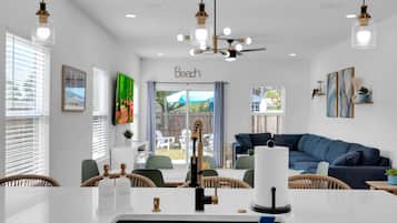 A modern kitchen with a central island, white cabinetry, and a dining area with wicker chairs.