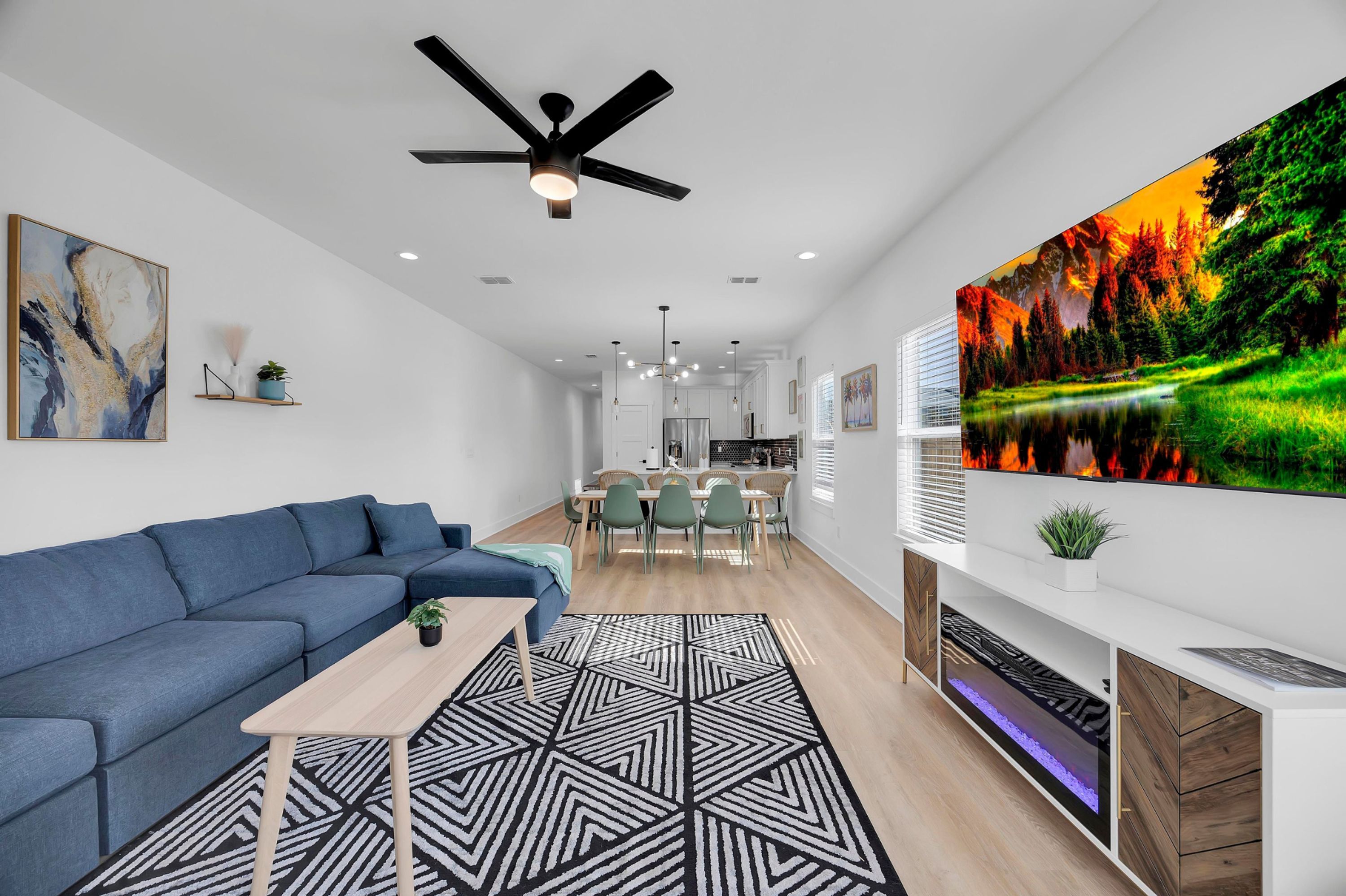 A modern living room with a blue sofa, a geometric rug, a ceiling fan, and a large TV displaying a nature scene.