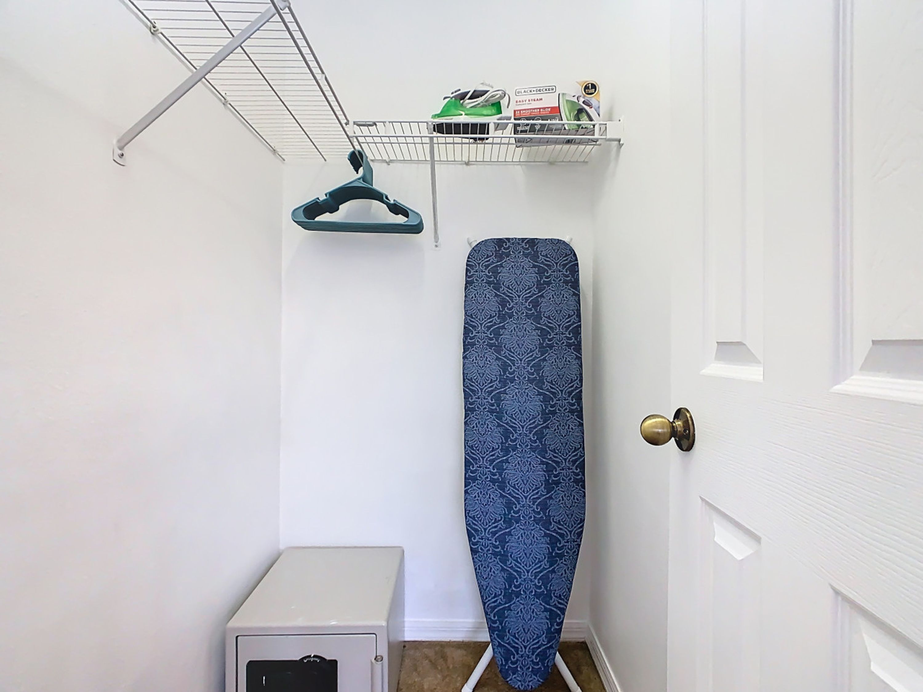A small room with a white door, a white cabinet, and a wall-mounted drying rack with clothes.