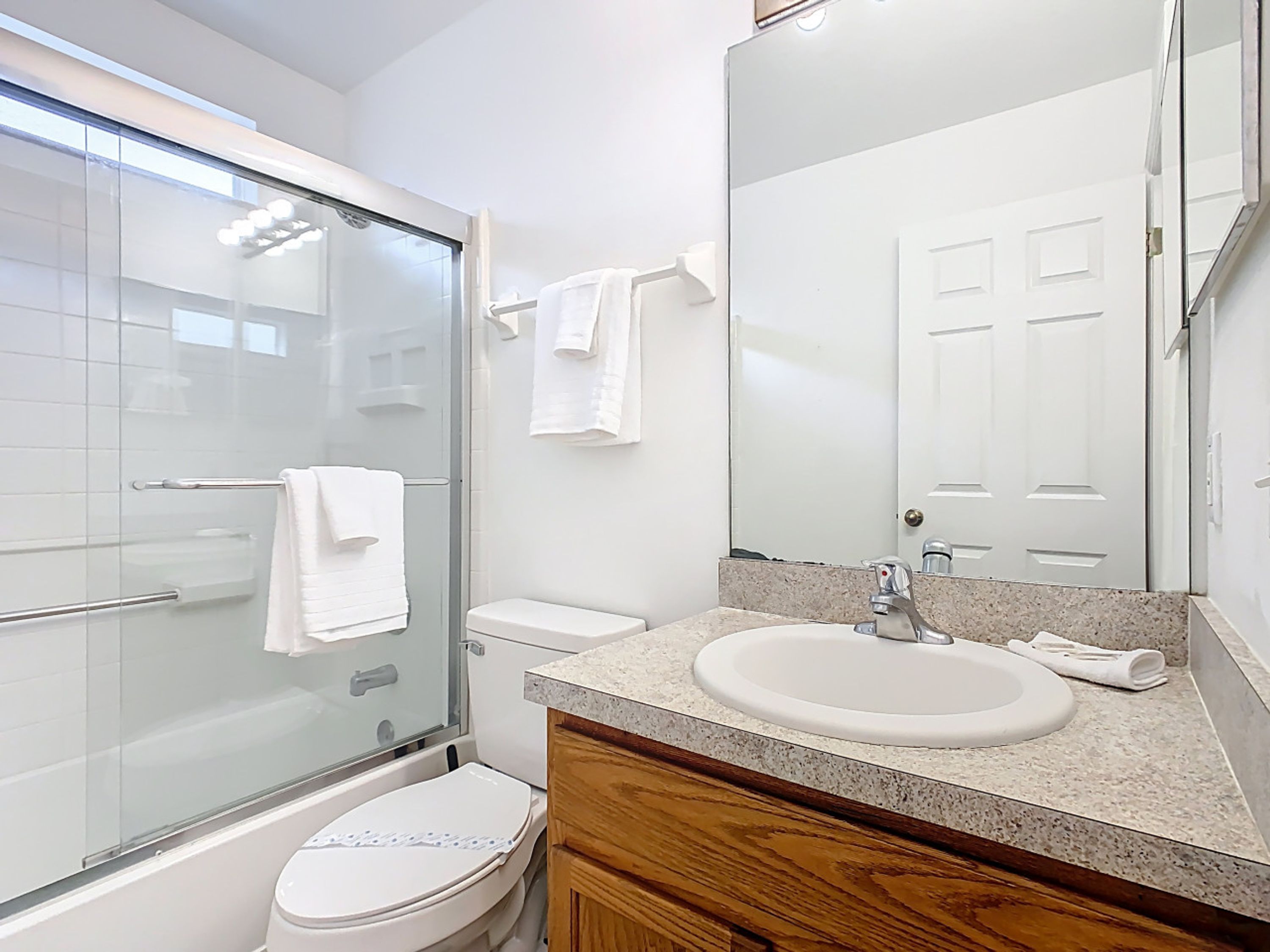 Un bagno moderno con box doccia in vetro, un water bianco, un lavabo con piano in granito e uno specchio grande.