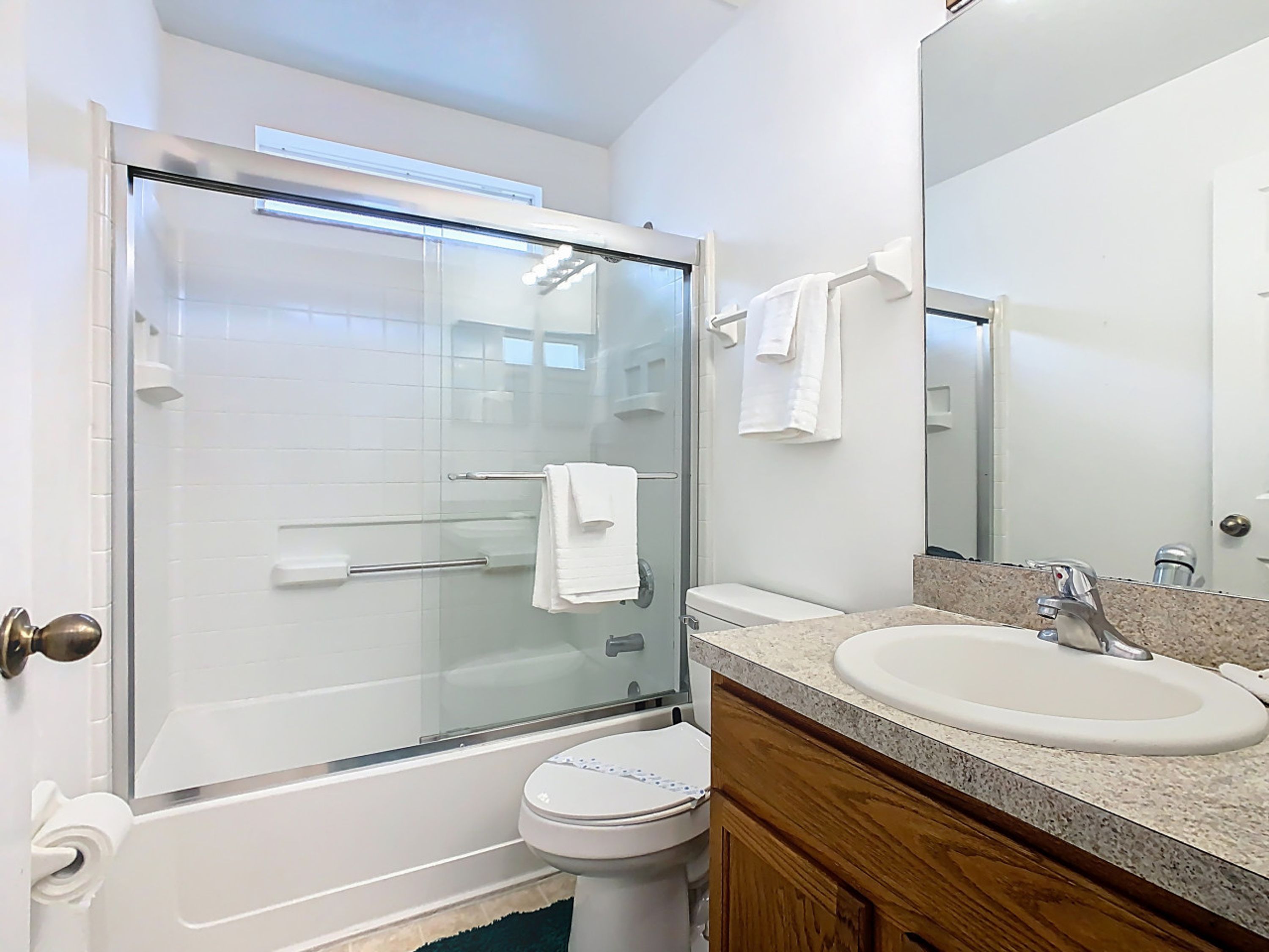 A bathroom with a glass-enclosed shower, a white toilet, a sink with a granite countertop, and a mirror.
