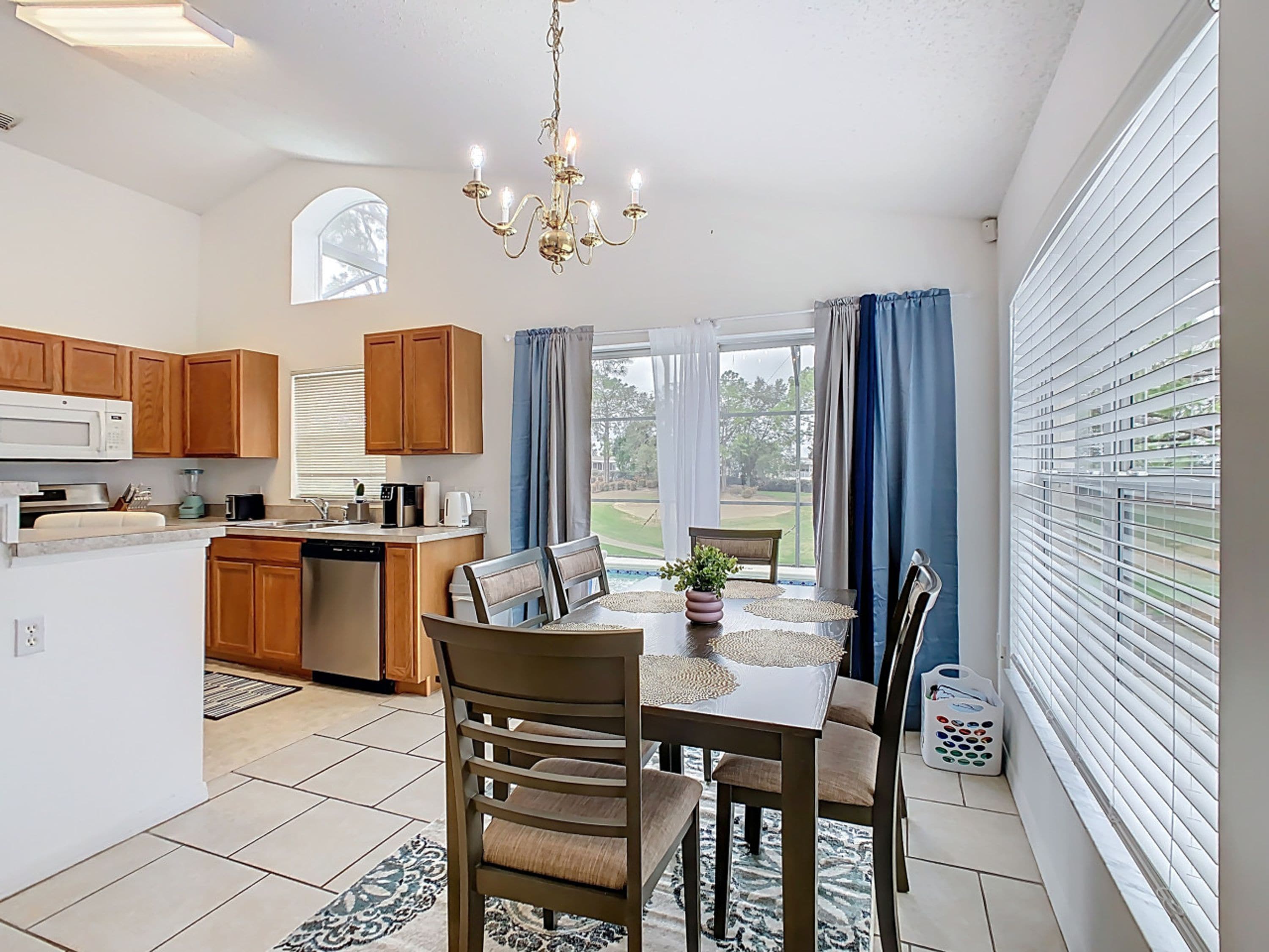 A modern kitchen with wooden cabinets, a dining area with a table and chairs, and a large window with curtains.