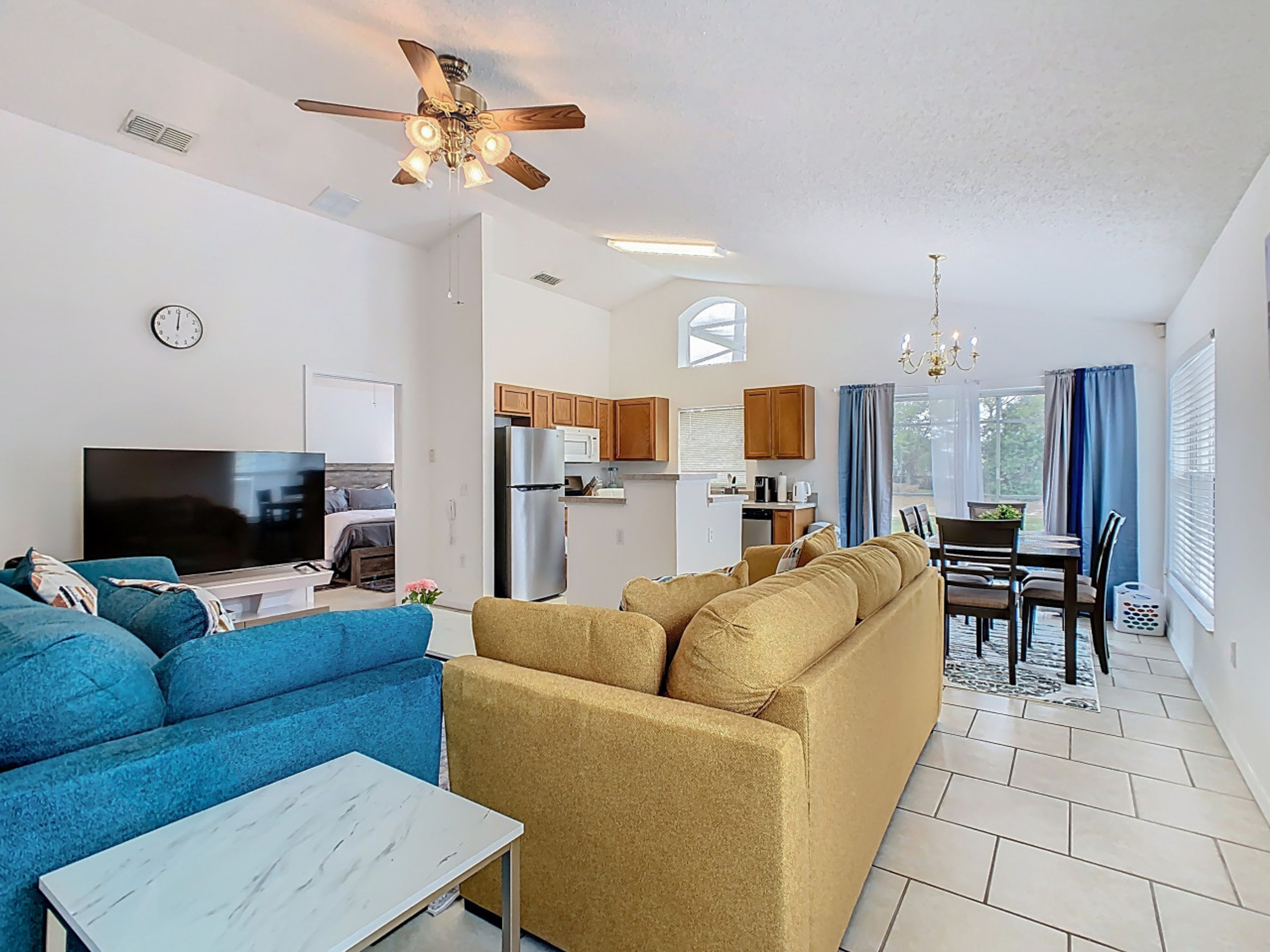 A modern living room with a blue sofa, a beige sofa, a TV, and a ceiling fan.