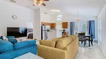 A modern living room with a blue sofa, a beige sofa, a TV, and a ceiling fan.