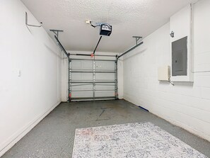 A garage with a closed metal door, a concrete floor, and a white wall with a window.