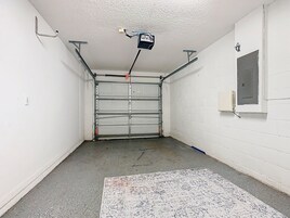 A garage with a closed metal door, a concrete floor, and a white wall with a window.