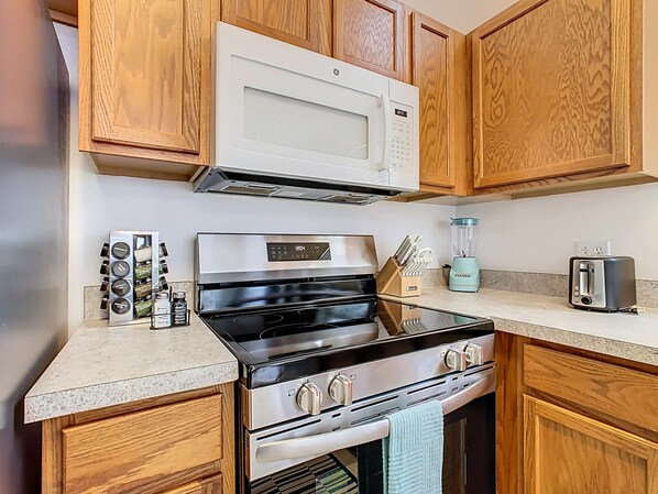 A kitchen with wooden cabinets, a stainless steel stove, a microwave, a toaster, and a blender.