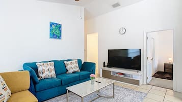 Una sala de estar con un sofá azul, una mesa de centro, un televisor de pantalla plana y un ventilador de techo.