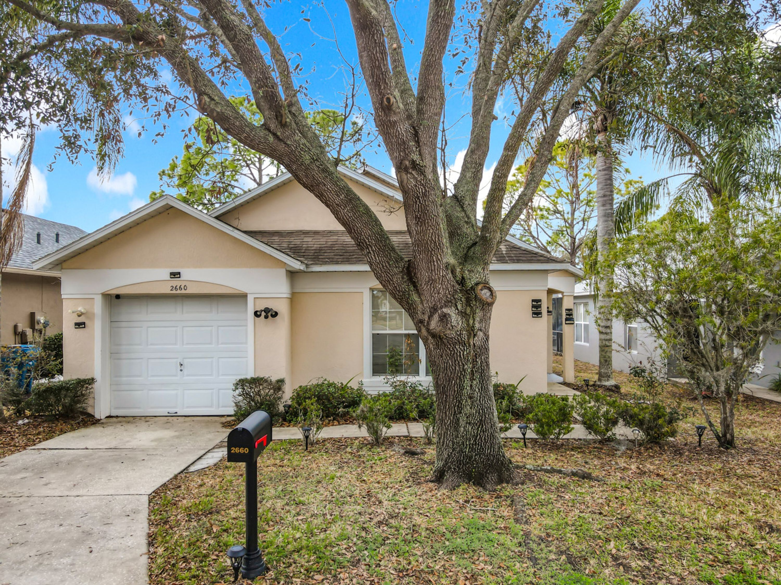 A residential house with a garage, a mailbox, and a large tree in the front yard.