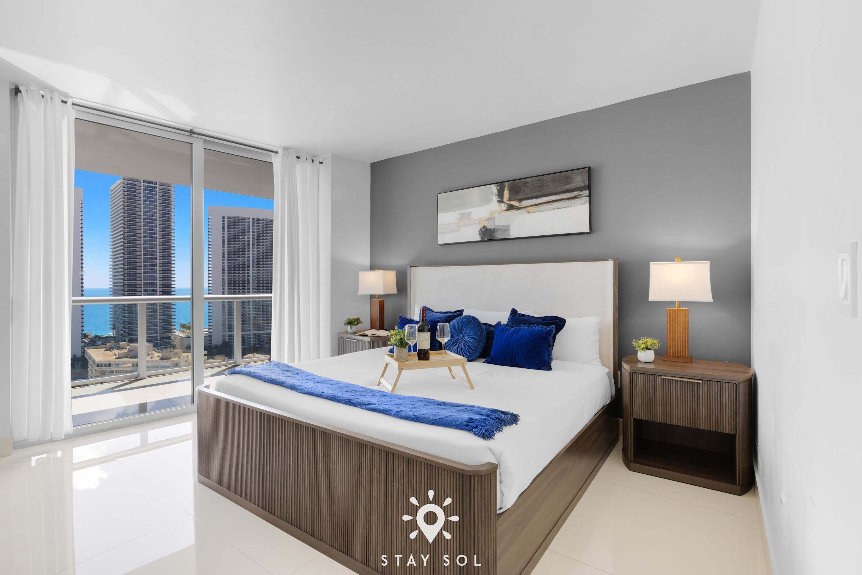 A modern hotel room with a large bed, two bedside tables, a view of the cityscape, and a balcony.