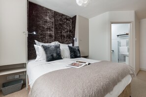A modern bedroom with a large bed, a dark textured headboard, and a view of a bathroom with a towel rack. - The Fox at Hurley - Stunning Boutique B B (Maidenhead)