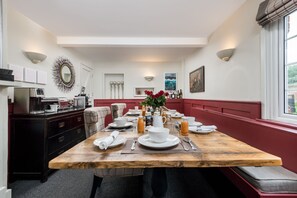 A dining area with a wooden table set for four, flanked by red cushioned benches. - The Fox at Hurley - The Warren Suite (Maidenhead)