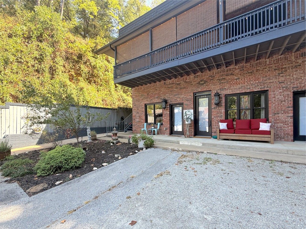 A brick building with a balcony, outdoor seating, and a gravel driveway.