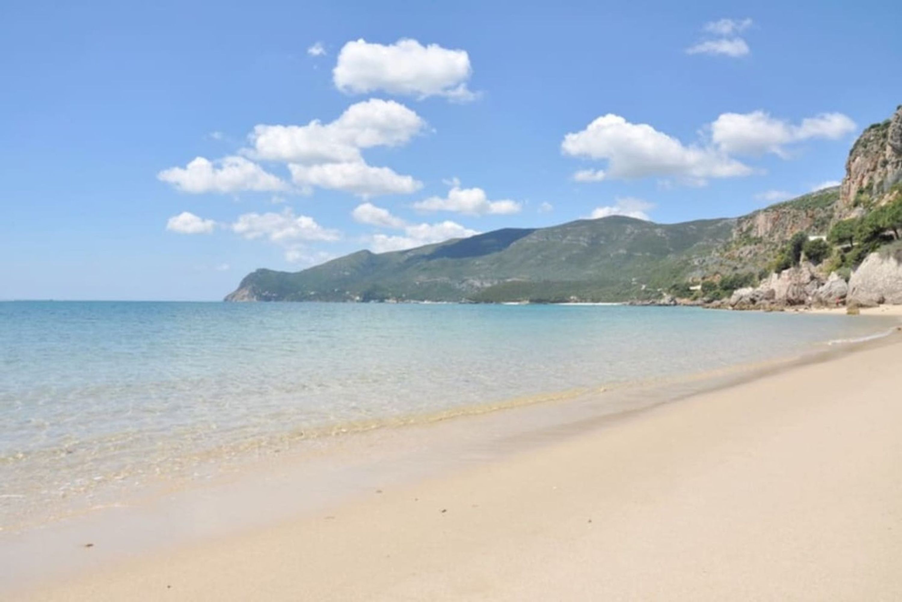 Una playa con agua cristalina, una orilla arenosa y una montaña al fondo.