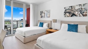 Ein Hotelzimmer mit zwei Betten, einem Schreibtisch, einem Stuhl und Blick auf die Stadt.
