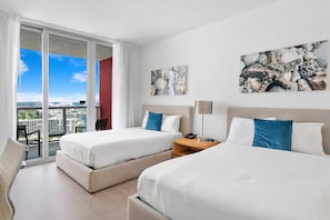Quarto de hotel com duas camas, uma escrivaninha, uma cadeira e vista para a cidade.