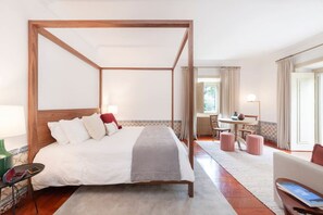 Ein Hotelzimmer mit Himmelbett, Schreibtisch, Sessel und einer Couch.