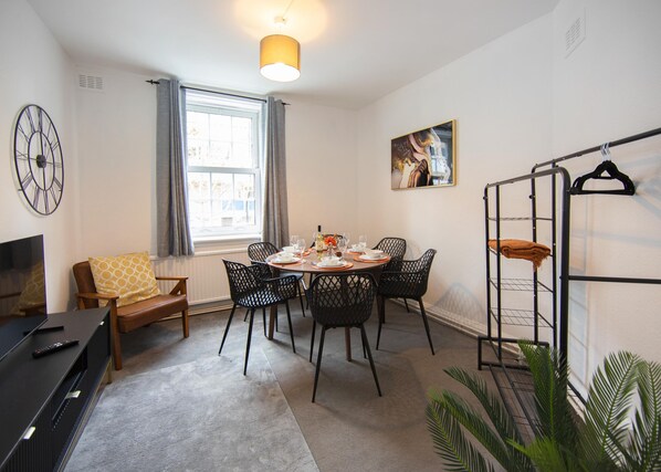 A dining area with a round table, chairs, a TV, and a window with curtains. - Portobello Executive Residence - Free Wifi (London)