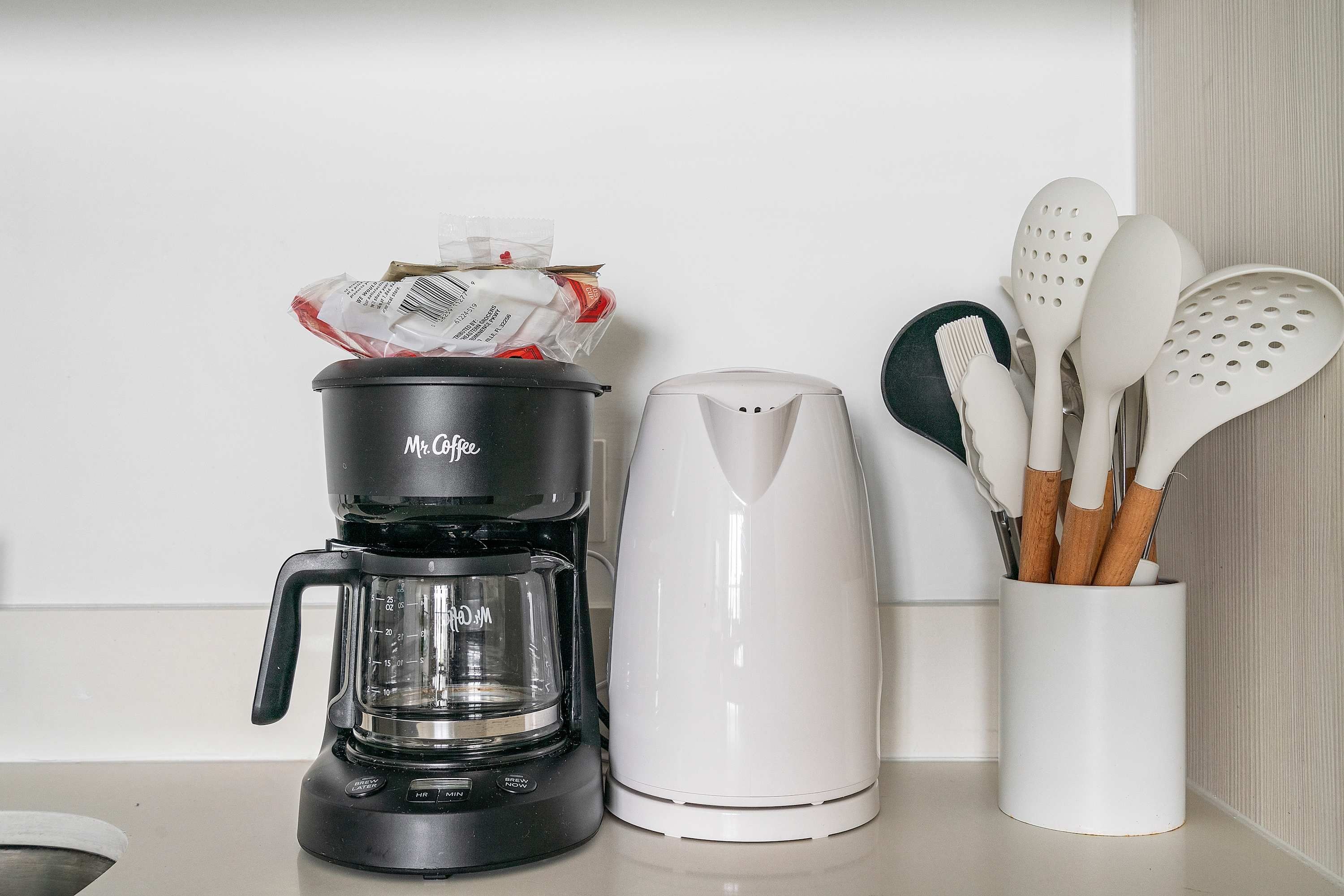 A kitchen counter with a coffee maker, a kettle, and a utensil holder.