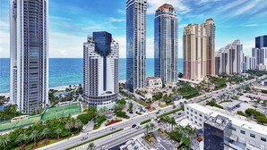 A high-rise urban area with modern architecture, a clear sky, and a view of the ocean. - Oceanview Studio Pool Beach Dining Miami (Sunny Isles Beach)