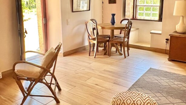 Una habitación con techo de madera, una mesa de comedor con sillas, un otoman decorado y un ventanal con vistas.