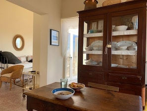 A dining area with a wooden table, wicker chairs, a cabinet with glass doors, and a bed with pillows. - Place of Grace in Lefkara (Pano Lefkara)