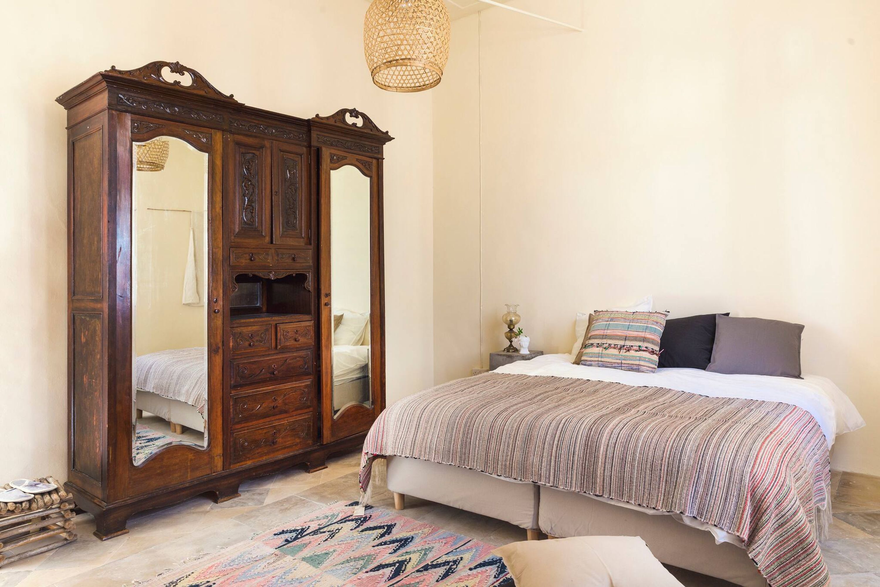 Un dormitorio con un amplio armario de madera, una cama con manta a rayas y una alfombra tejida.
