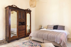 A bedroom with a large wooden wardrobe, a bed with a striped blanket, and a woven rug. - Place of Grace in Lefkara (Pano Lefkara)