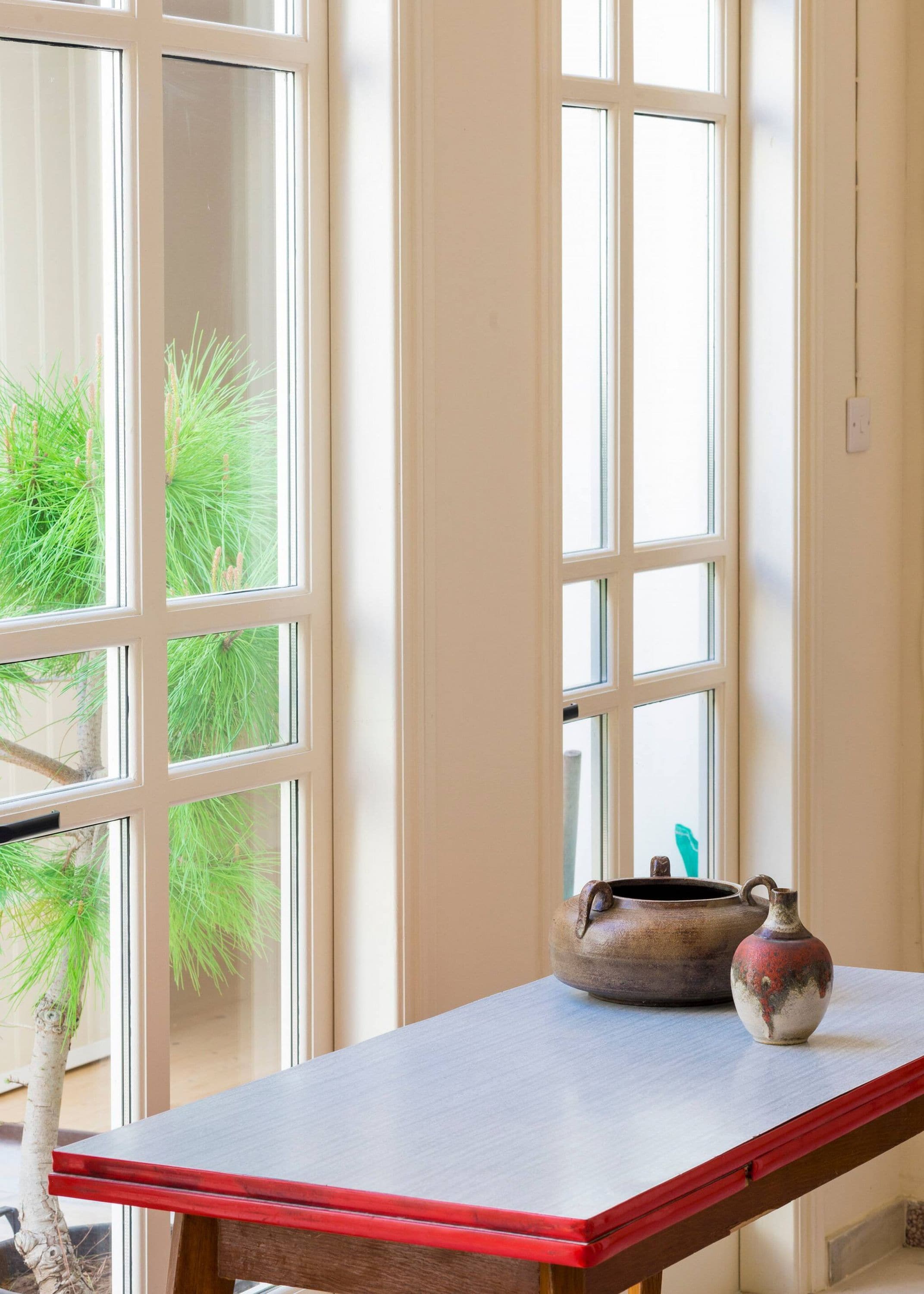 A room with a large window, a table with a red edge, and a potted plant.