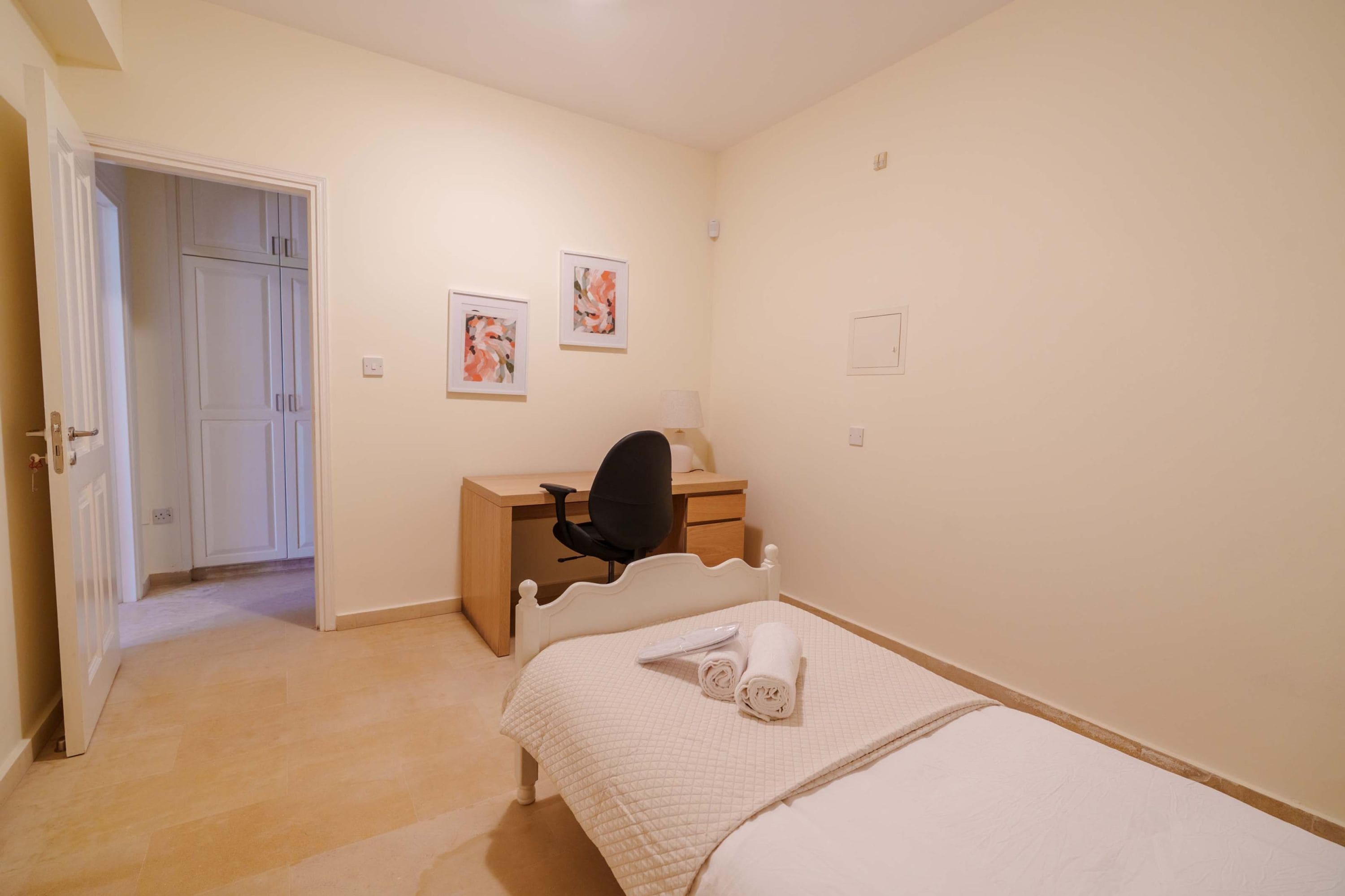 A bedroom with a bed, a desk, and a chair. There is a door leading to another room.