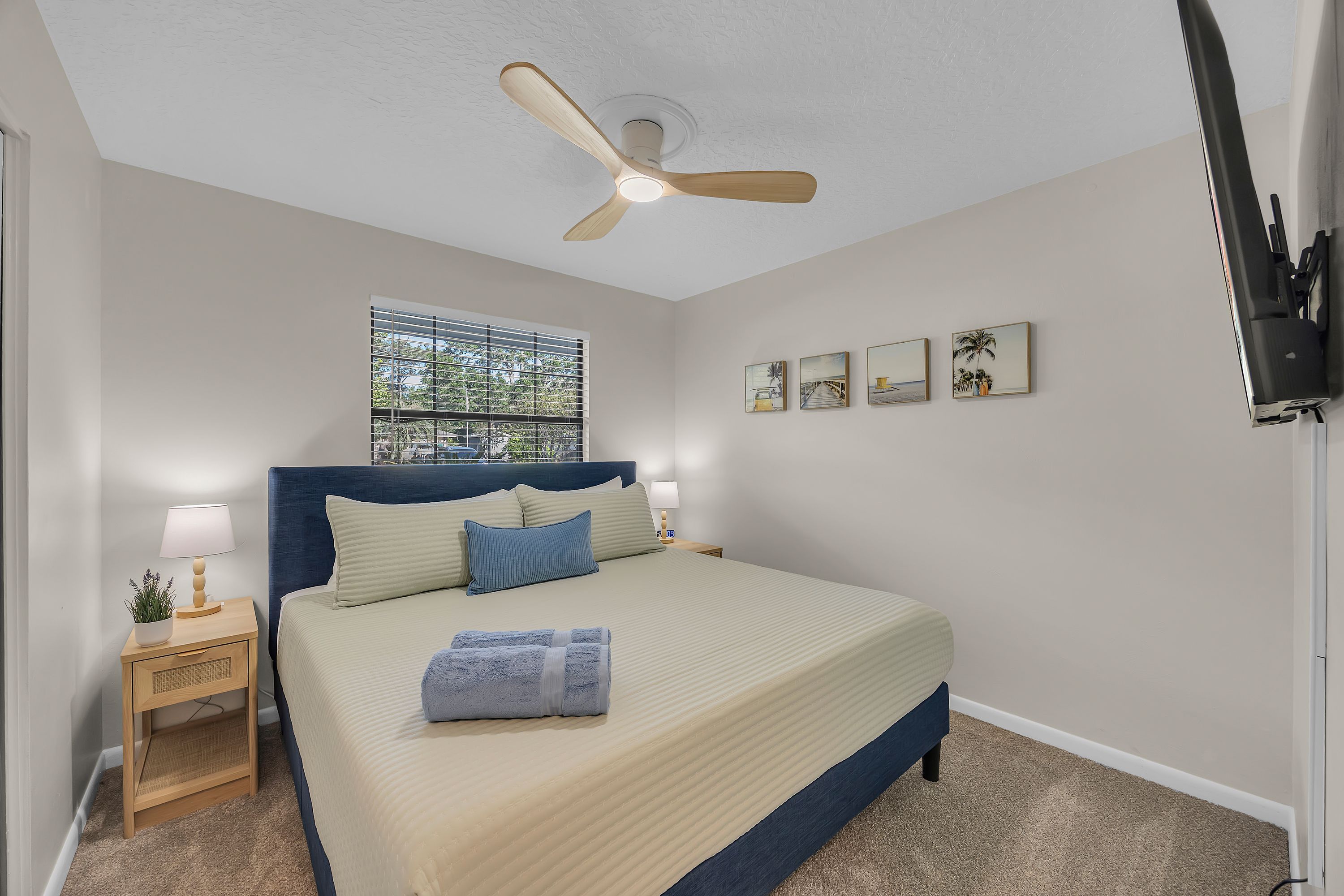 Un dormitorio con cama, ventilador de techo, ventana con persianas y decoración en la pared.