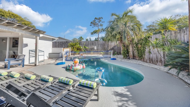 A backyard with a swimming pool, lounge chairs, and a wooden fence. - Endless Summer- Beach Pool Firepit 3 King Beds (Ponte Vedra Beach)