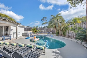 A backyard with a swimming pool, lounge chairs, and a wooden fence.