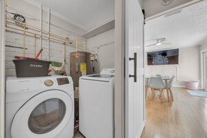 Un cuarto de lavado con lavadora y secadora Samsung, calentador de agua Rheem y ventilador de techo.