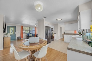 A modern kitchen with a built-in oven, a coffee machine, and a dining area with a round wooden table and white chairs. - Endless Summer- Beach Pool Firepit 3 King Beds (Ponte Vedra Beach)