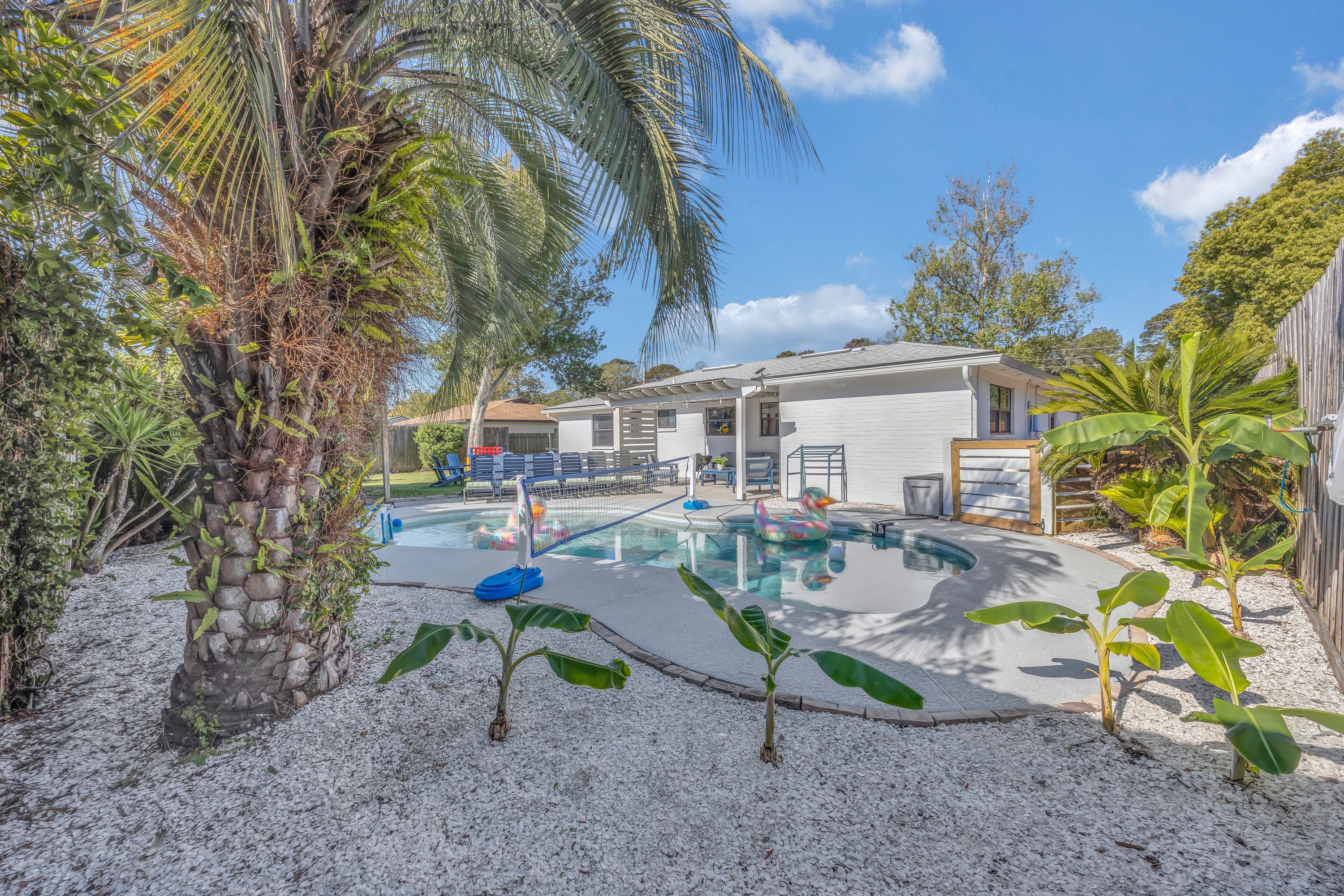 A residential backyard with a swimming pool, a wooden deck, and a house.