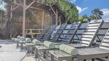Een rij ligbedden met handdoeken, een houten pergola en een heldere lucht.