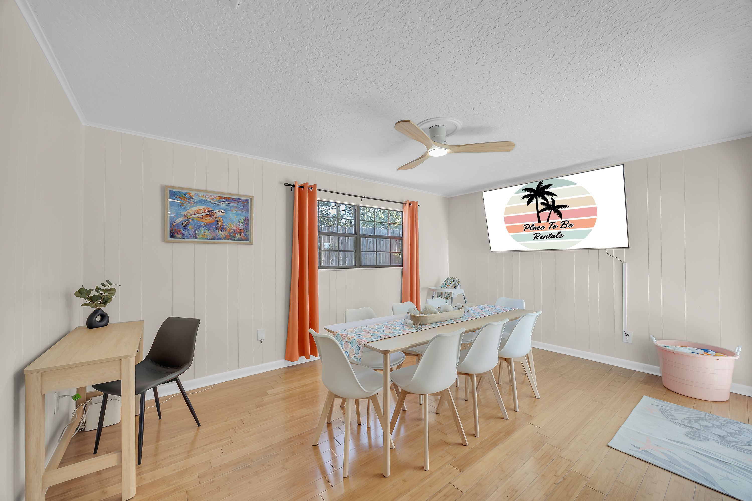 A dining area with a table, chairs, a ceiling fan, and a window with curtains.