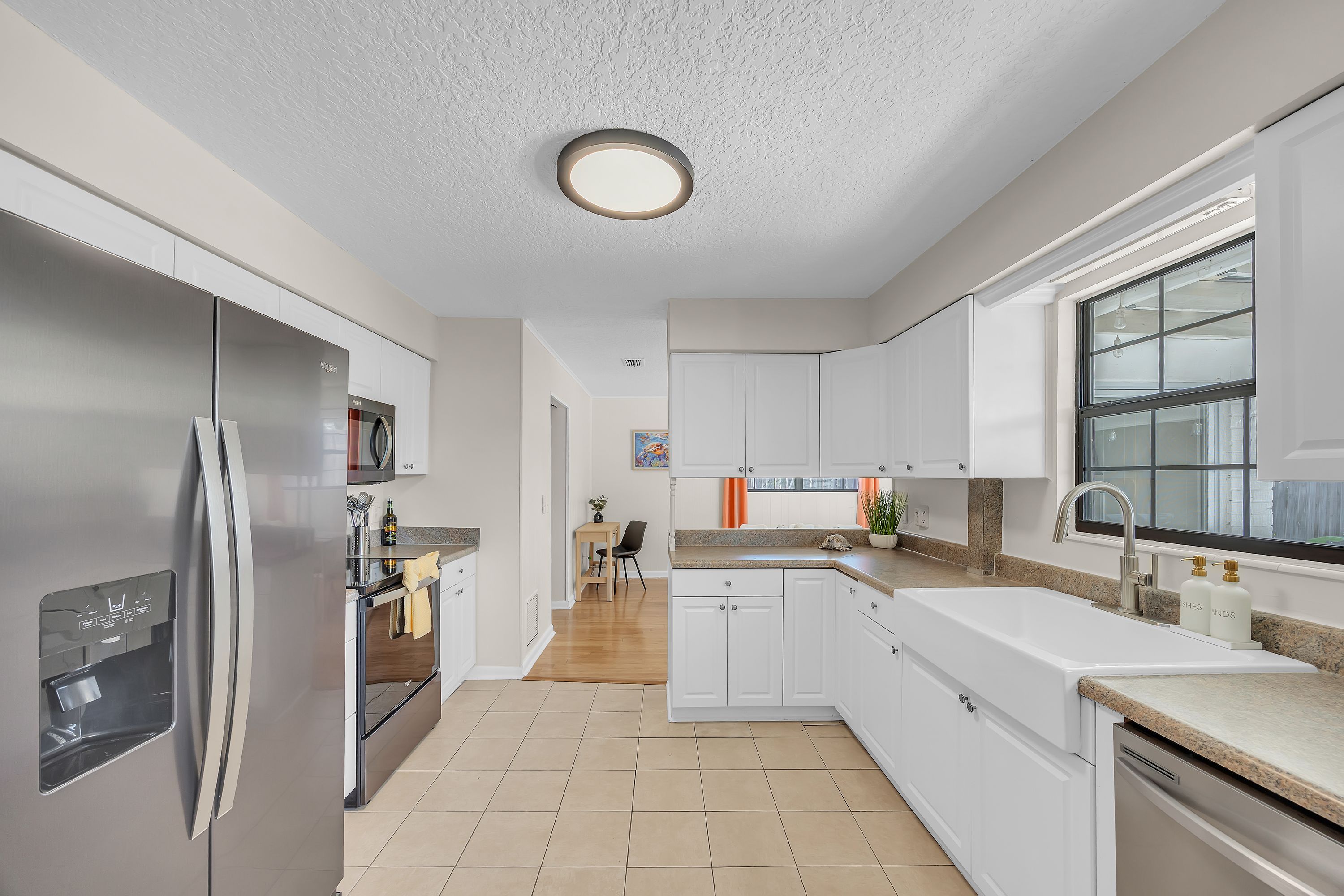 A modern kitchen with white cabinetry, a stainless steel refrigerator, and a window with a view.