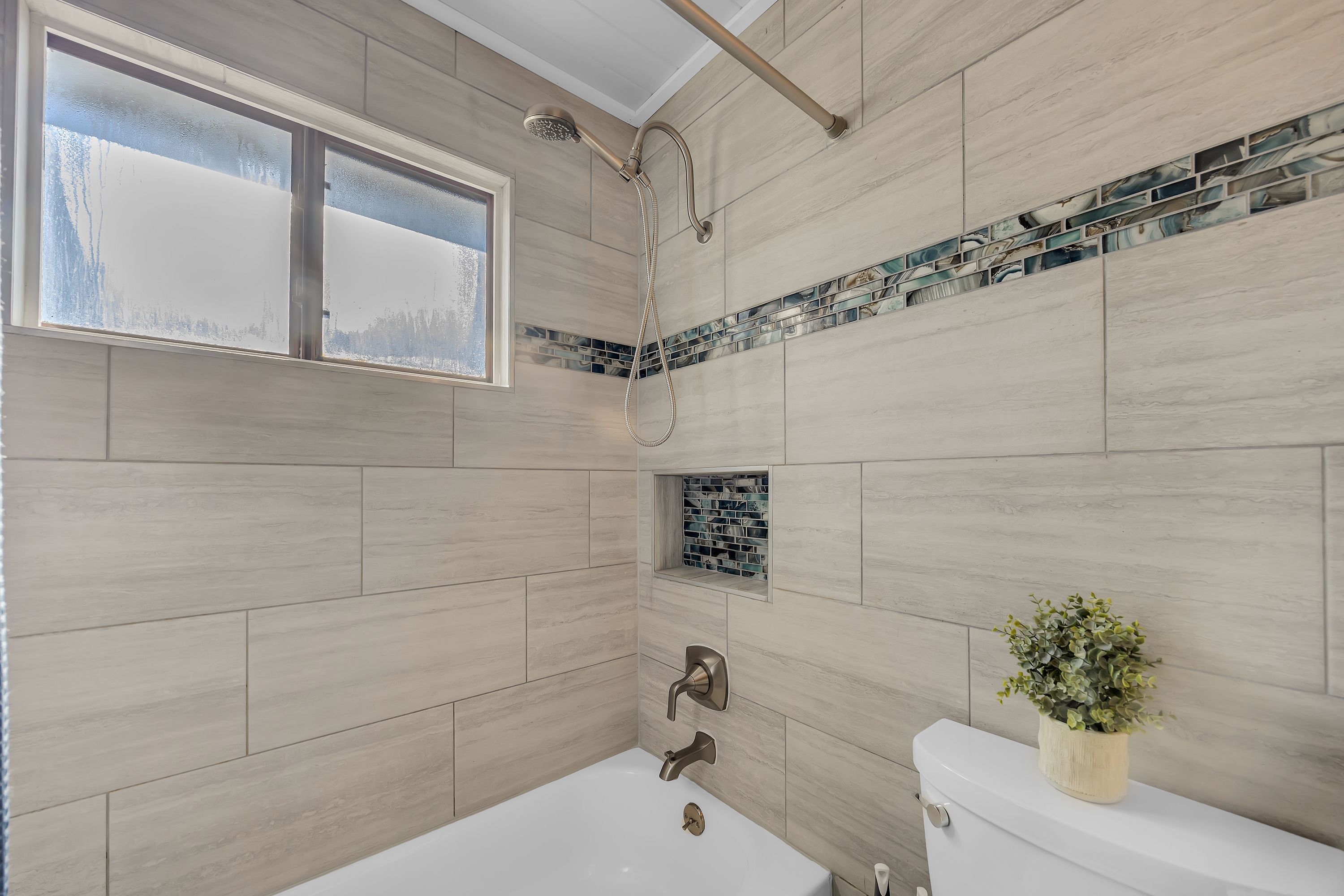 A bathroom with a bathtub, a toilet, a shower, and a window.