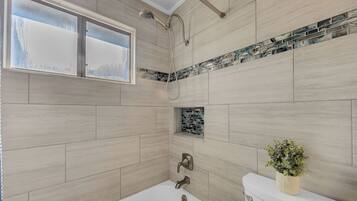 A bathroom with a bathtub, a toilet, a shower, and a window.