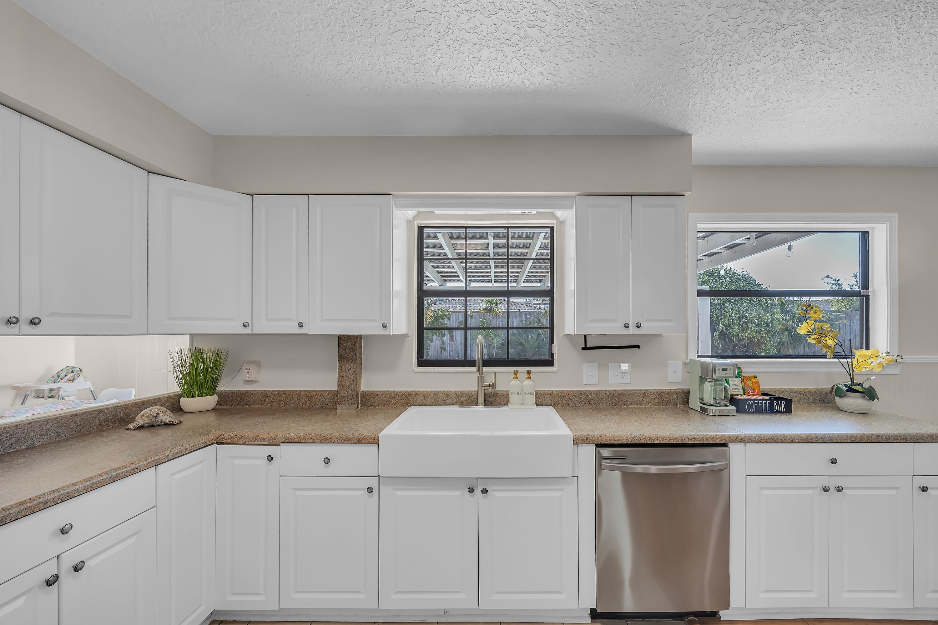 A kitchen with white cabinets, a granite countertop, a stainless steel dishwasher, and a window with a view of the outdoors.