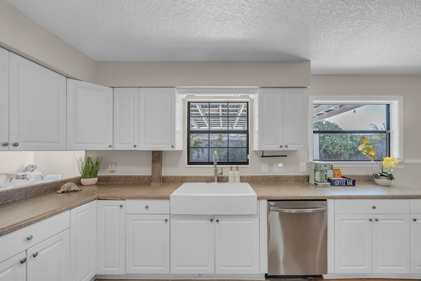 A kitchen with white cabinets, a granite countertop, a stainless steel dishwasher, and a window with a view of the outdoors.