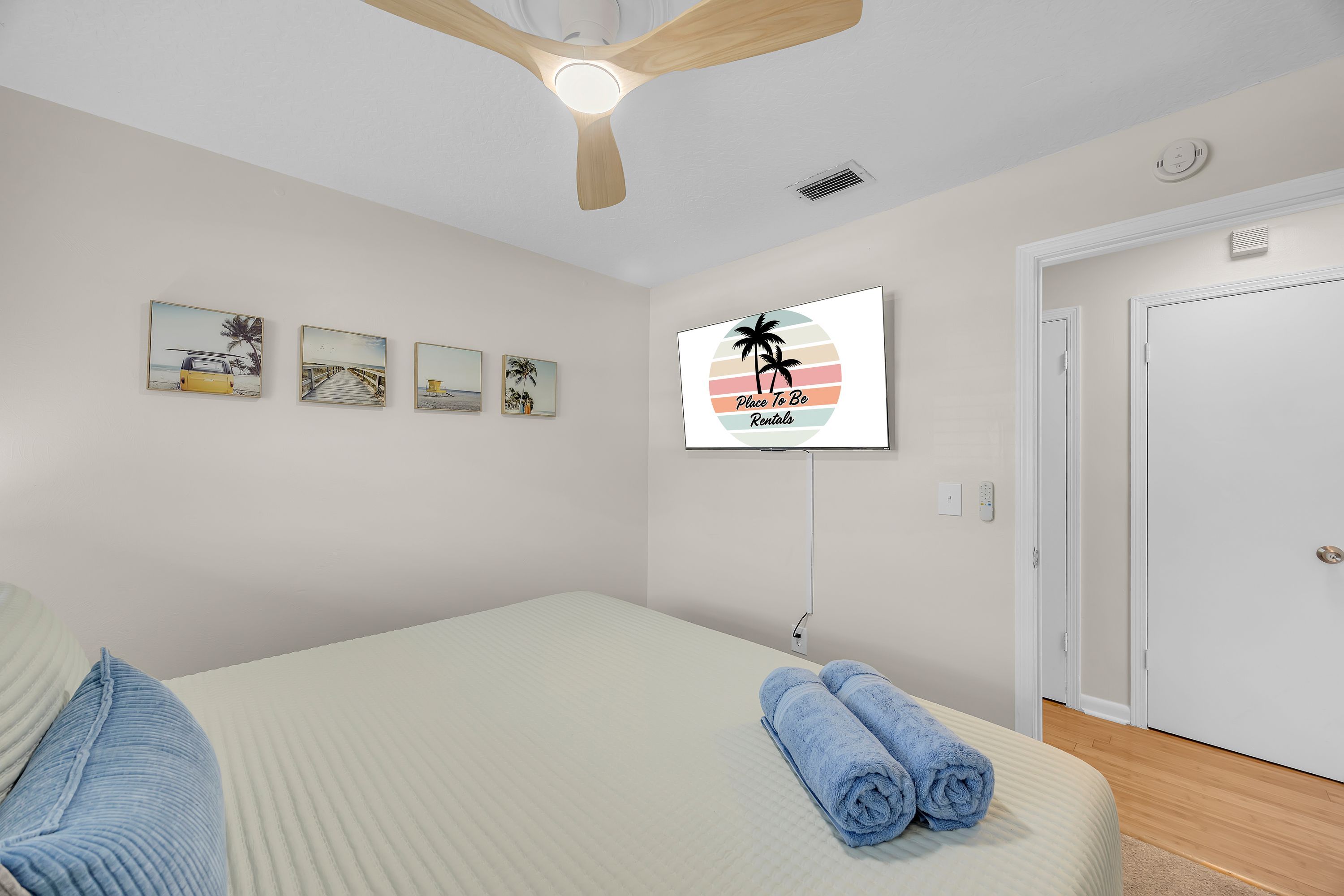 Een slaapkamer met een bed, een plafondventilator, een tv aan de muur en een deur.