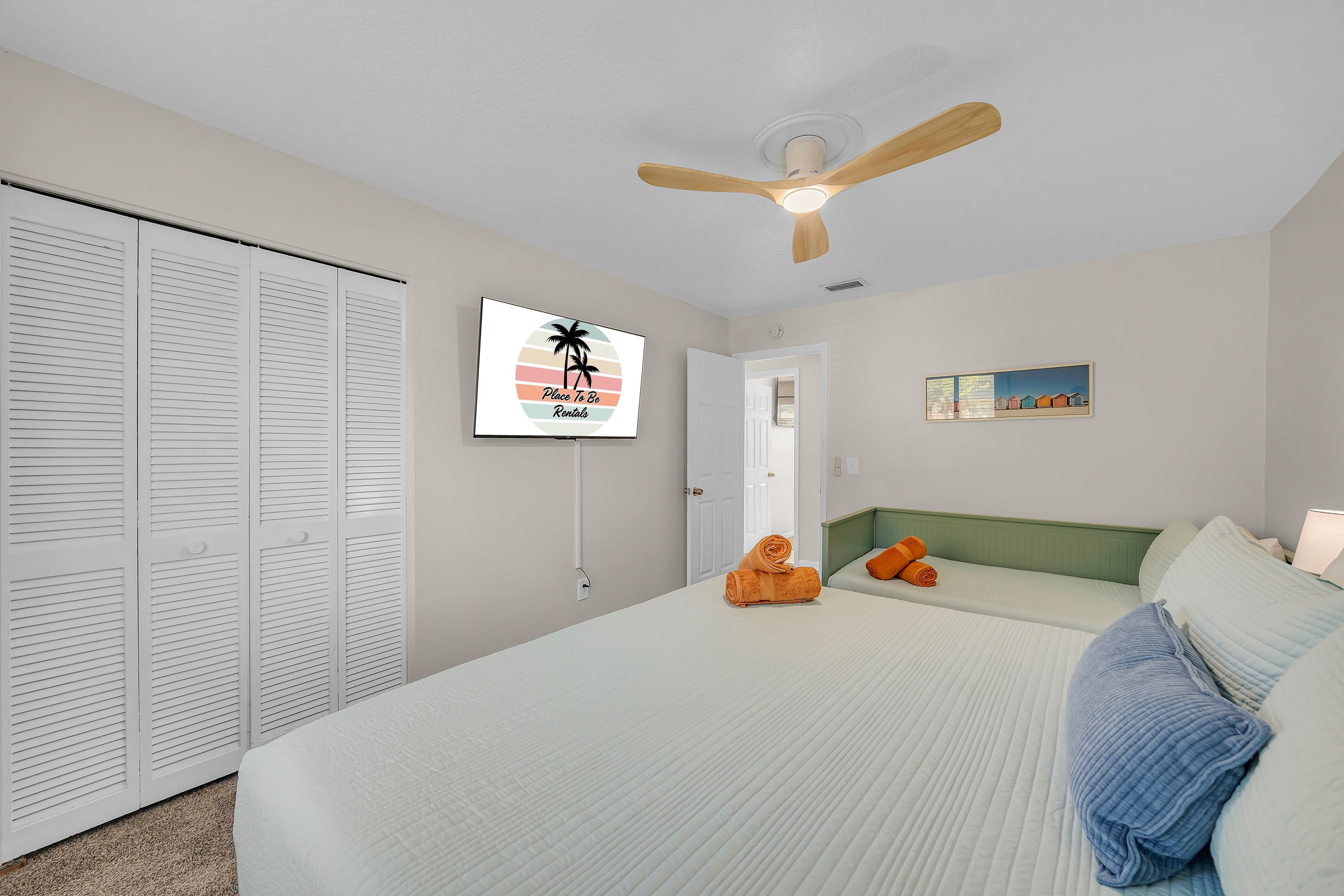 A bedroom with a bed, a ceiling fan, a TV, and a painting on the wall.