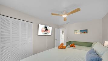 A bedroom with a bed, a ceiling fan, a TV, and a painting on the wall.