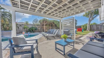 An outdoor patio with a pool, lounge chairs, and a pergola structure.