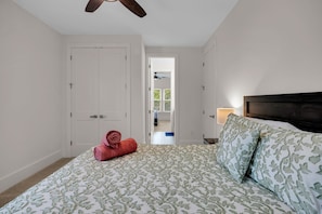 A bedroom with a bed, a door, a ceiling fan, and a view of a balcony.