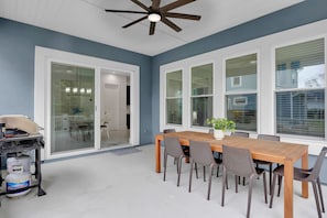 A dining area with a wooden table and chairs, large windows, and a ceiling fan.