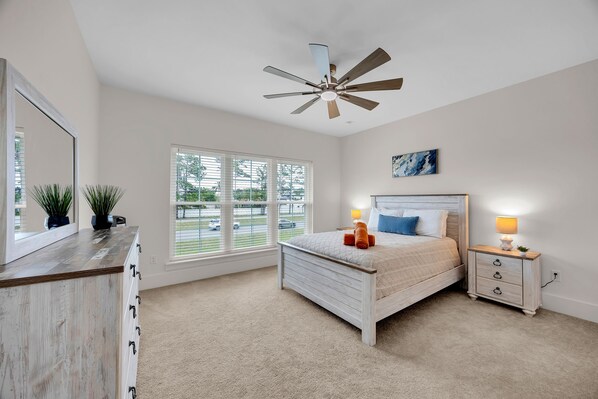 A bedroom with a bed, bedside tables, a ceiling fan, a window with blinds, and a painting on the wall.